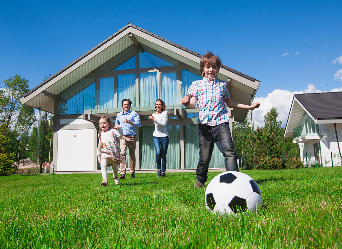 About Our Agency - Happy Family Running in Their Backyard Playing Soccer