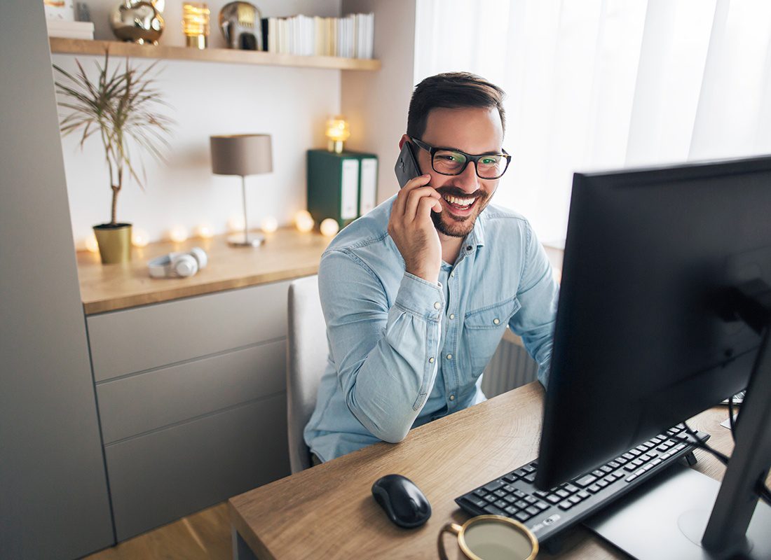 Contact - Friendly Man Smiling and Talking on the Phone at His Work Station at Home
